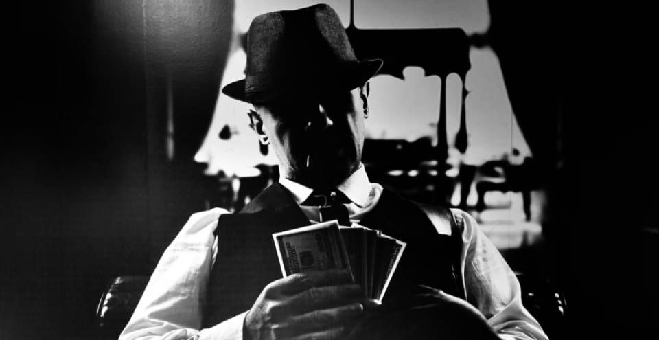 Mustavalkokuva pokeria pelaavasta miehestä klassisessa puvussa